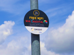 Blauer HImmel mit Wolken, davor ein Pfosten mit einem runden Schild mit Hinweisen zu freiem Wlan