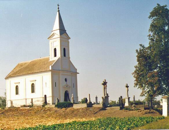 Kirchengemeinde, von der Seite das Kirchenschiff, davor der Friedhof mit einigen Gräbern, rechts ein Baum