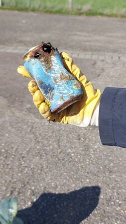 Hand mit Handschuh hält verostete Cola-Dose, Hintergrund grauer Asphalt