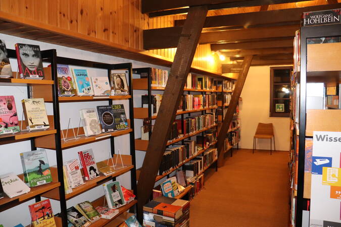 Gang in Bücherei Jöhlingen, schräg von vorne links nach hinten rechts, an der Wand Bücherregale, an der Decke und an der Wand Balken und eine Holzvertäfelung