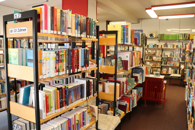 Gang in Bücherei Wössingen, schräg von vorne links nach hinten rechts, im Vordergrund und im Hintergrund viele Bücherregale