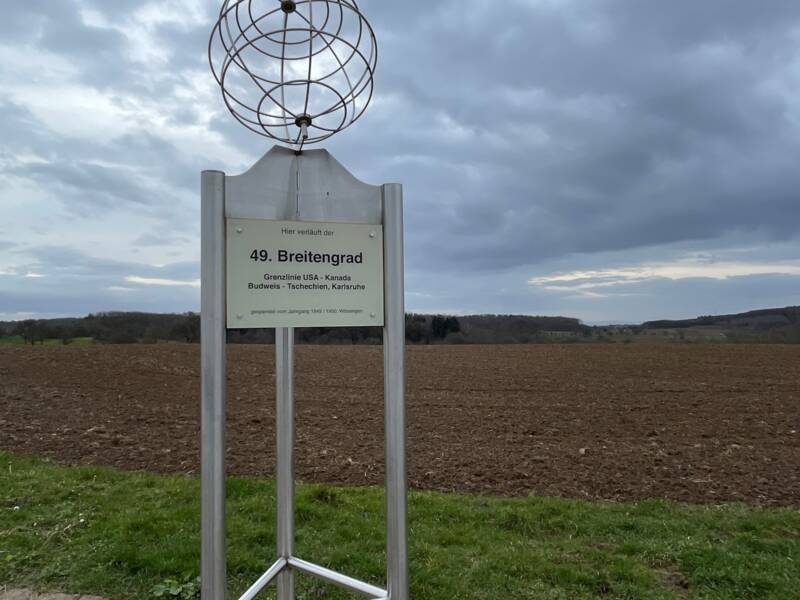 Informationsschild über den 49. Breitengrad auf einem Feld.