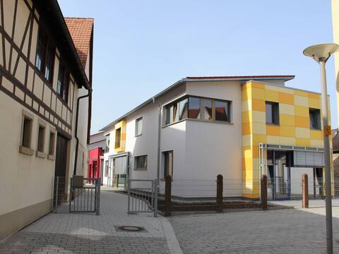 Modernes Kitagebäude, seitlich im Vordergrund ist die Außenwand des Speyerer Hofes zu sehen, diese ist im Fachwerkhausstyle.