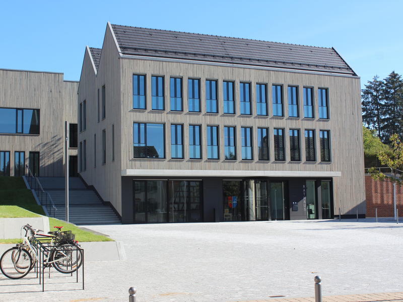 Großes Rathaus mit einem großen Rathausvorplatz, links Fahrräder und rechts hinten Bäume.