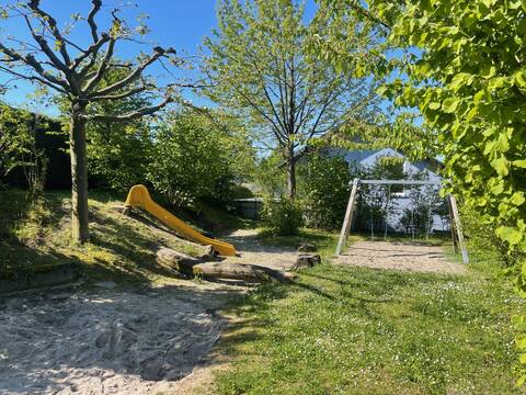 Bild einer Schaukel, einer Rutsche und eines Sandspielfeldes auf dem Spielplatz in der Mozartstraße