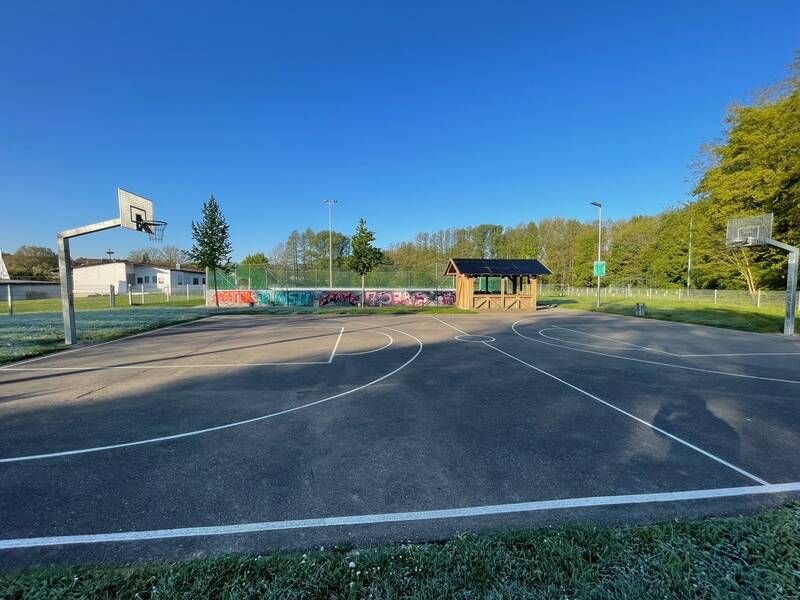 Bild eines Minispielfeldes für Ballsportarten im Ortsteil Wössingen. Im Hintergrund ist eine Holzhütte zu sehen.