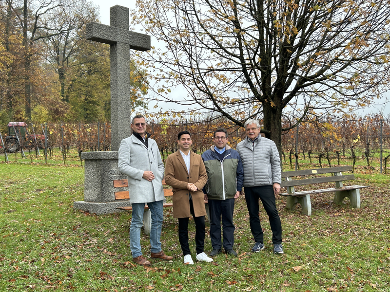 Pfarrer Maiba, Bürgermeister Özcan, Karl-Heinz Burgey und Gerd Eberle stehen vor dem renovierten steinernen Kreuz, im Hintergrund sind Weinreben