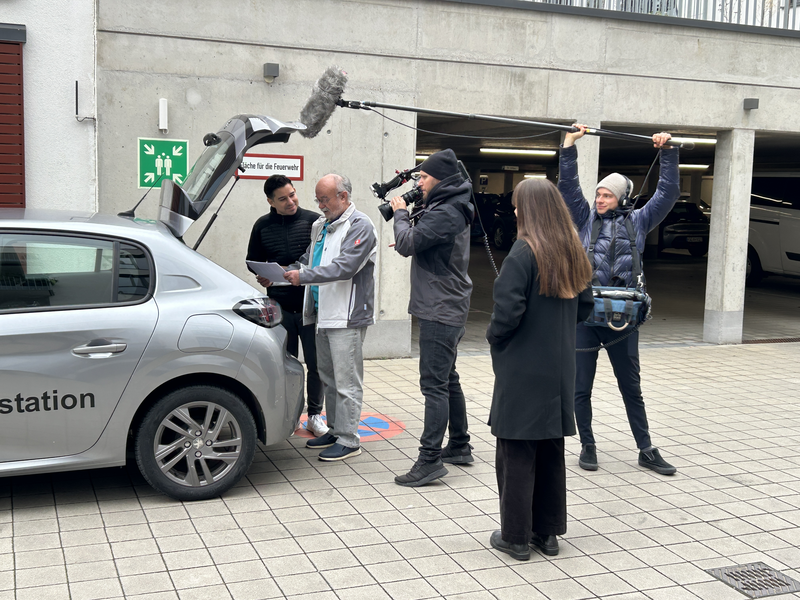 ein Fernsehteam von RTL steht mit Bürgermeister Özcan vor dem geöffneten der AWO.Auto 