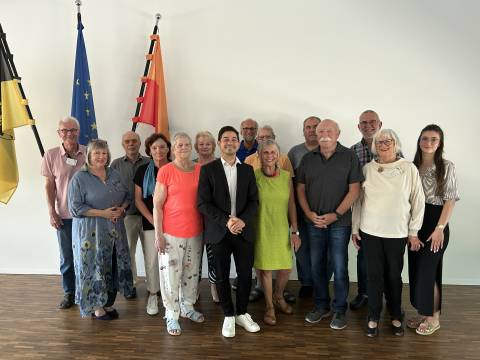 Gruppenbild des Seniorenbeirats 2024 mit Bürgermeister Özcan in der Mitte und Sozialarbeiterin Nadine Wipfler rechts am Rand. Die Gruppe steht im Ratssaal des Rathauses vor den drei Fahnen von Baden-Württemberg, Europa und Walzbachtal