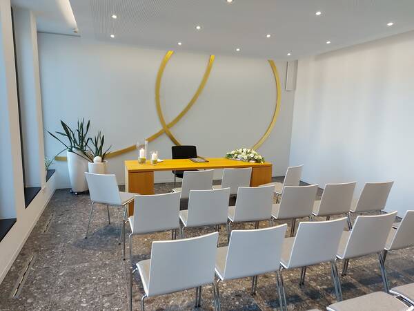 Blick von links in das Trauzimmer im Rathaus Wössingen. Stühle stehen im Vordergrund. Im Hintergrund der Trausekretär und goldene Ringe an der Wand.