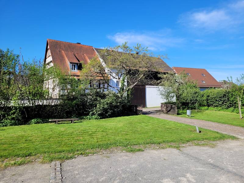 Garten im hinteren Bereich des Wössinger Hofs. Im Hintergrund stehen Häuser. Ein großer Baum ist zu sehen.