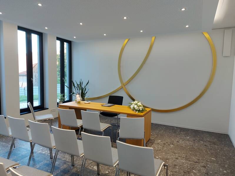 Blick von rechts in das Trauzimmer im Rathaus Wössingen. Stühle stehen im Vordergrund. Im Hintergrund der Trausekretär und goldene Ringe an der Wand.