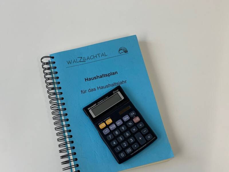 gebundener Haushaltsplan mit blauem Umschlag auf dem ein schwarzer Taschenrechner liegt