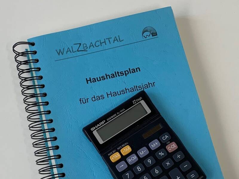 gebundener Haushaltsplan mit blauem Umschlag auf dem ein schwarzer Taschenrechner liegt