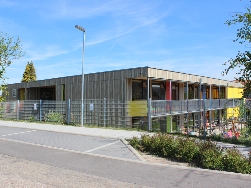 Außenansicht Kinderhaus Regenbogen. Holzfassade mit bunten Elementen, außen herum ein Zaun