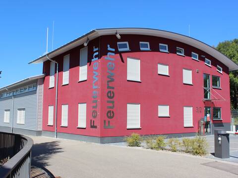 Feuerwehrhaus Wössingen mit grau roter Fassade. Davor Hofeinfahrt mit Schranke. Links daneben eine Straße