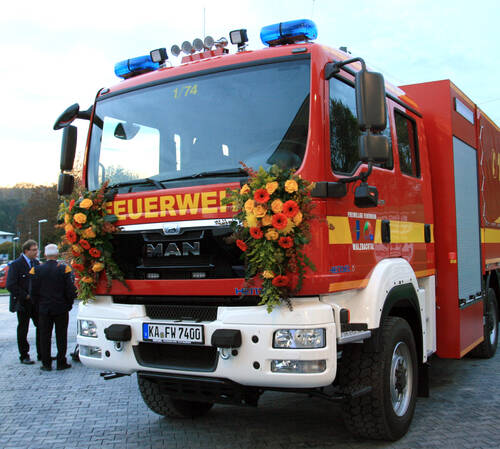 Rotes Feuerwehrauto mit gelber Aufschrift. Rechts und links am Auto sind Blumen angebracht. 
