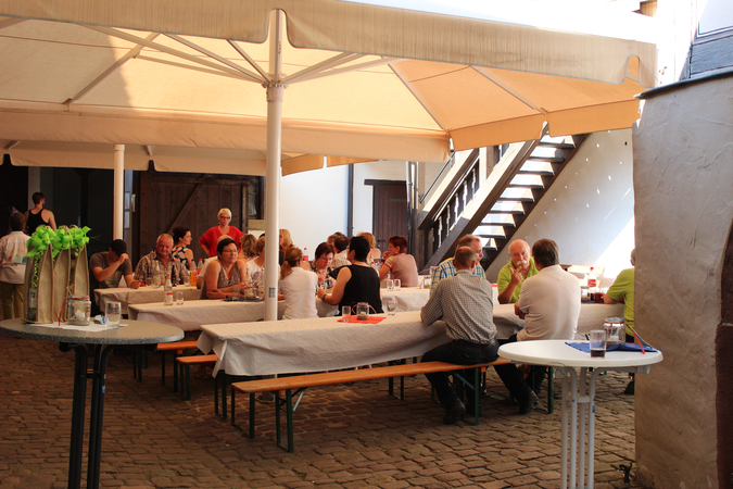 Innenhof des Speyerer Hofs, mit aufgestellten Sonnenschirmen. Darunter sieht man wie viele Menschen an Biertischen sitzen.