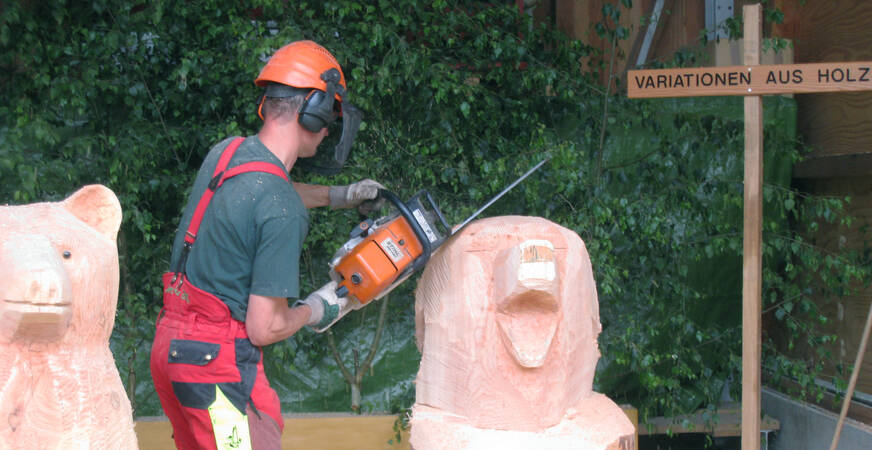 Mitarbeiter mit Kettensäge in der Hand, die eine Figur aus Holz erstellt