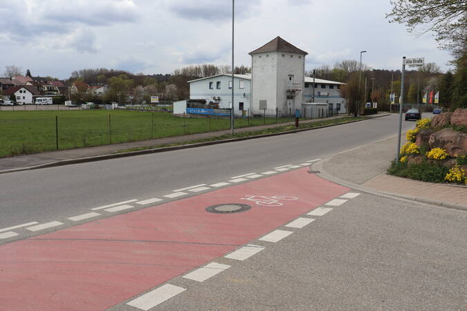 Wössinger Straße, auf dem Gehweg ist ein roter Weg für Fahrräder eingezeichnet mit einem Fahrrad-Symbolbild