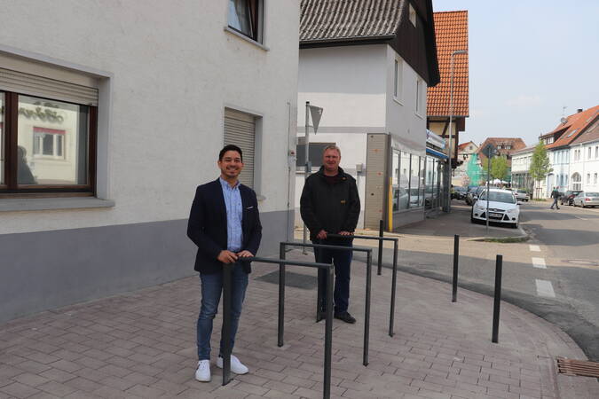 Herr Özcan und Herr Engel stehen neben drei Fahrradständern auf der Jöhlinger Straße