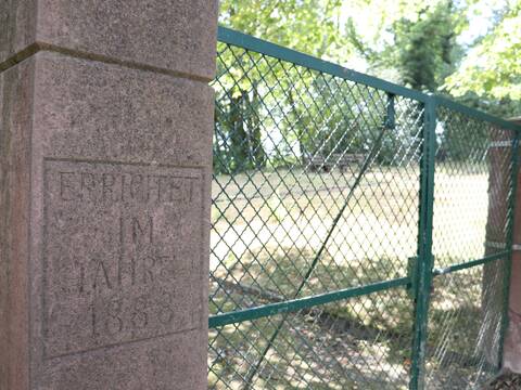 Eingang Jüdischer Friedhof. Links und Recht eine Mauer, dazwischen ein Zaun