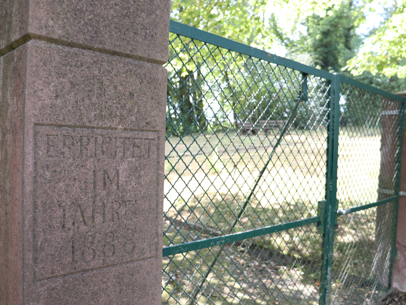 Eingang Jüdischer Friedhof. Links und Rechts eine Mauer, dazwischen ein Zaun