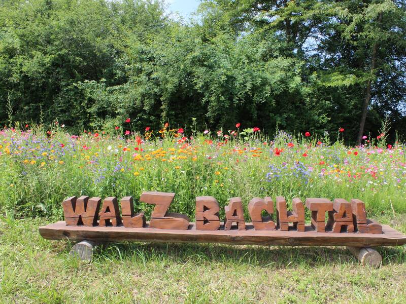 Walzbachtal Schriftzug aus Holz. Im Hintergrund eine Blumenwiese