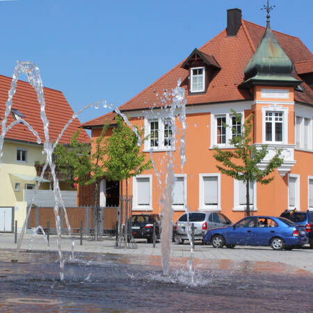 Brunnen auf dem Kirchplatz Jöhlingen, Dahinter ein Haus mit oranger Fassade