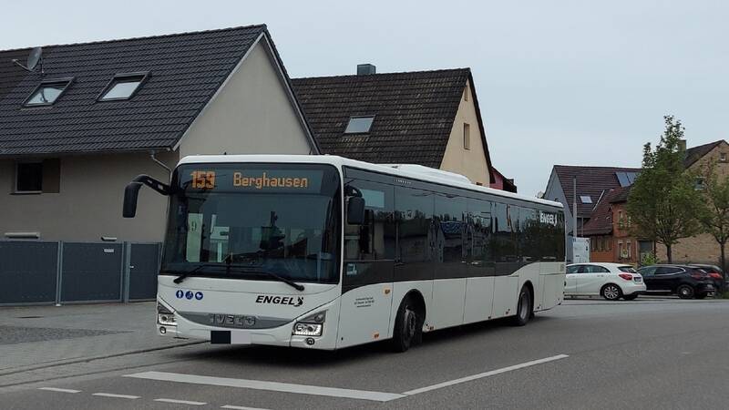weißer Linienbus an der Bushaltestelle Kirchplatz in Jöhlingen. Im Hintergrund stehen Fahrzeuge und Wohnhäuser