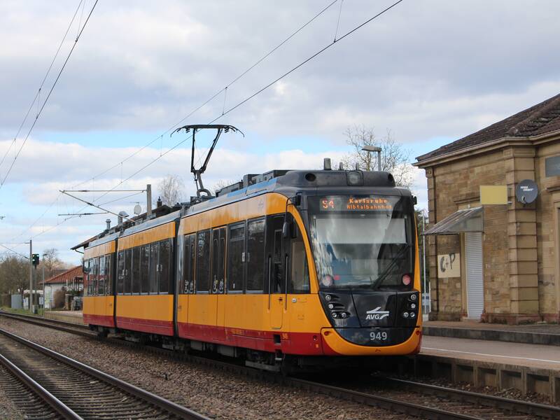 Straßenbahn S4 in gelb fährt auf dem Gleis. Daneben die Haltestelle
