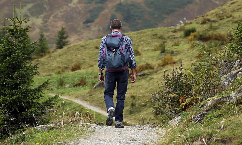 Mann wandert mit Rucksack durch hügelige Landschaft